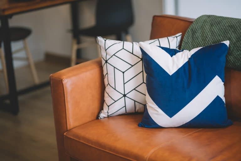 A white and blue throw pillows arranged on a brown leather sofa, Can You Dry A Pillow In The Dryer?