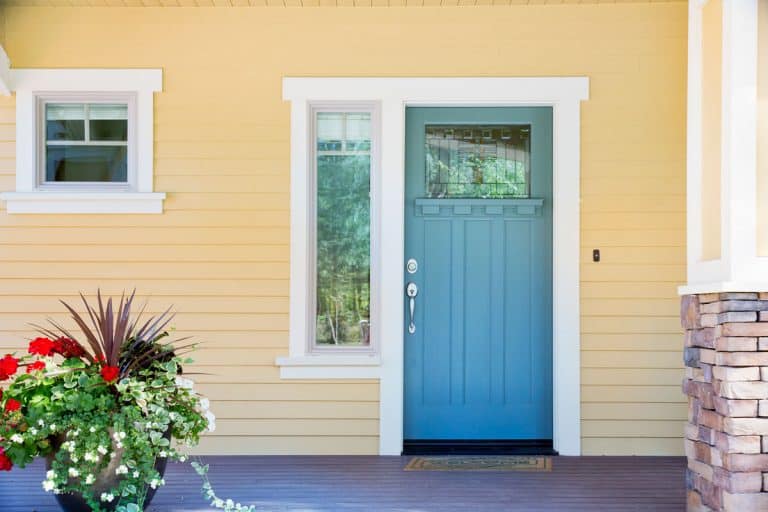 Front-porch-of-a-house-with-a-cream-colored-wooden-siding、-blue-front-door -and-plants-outside