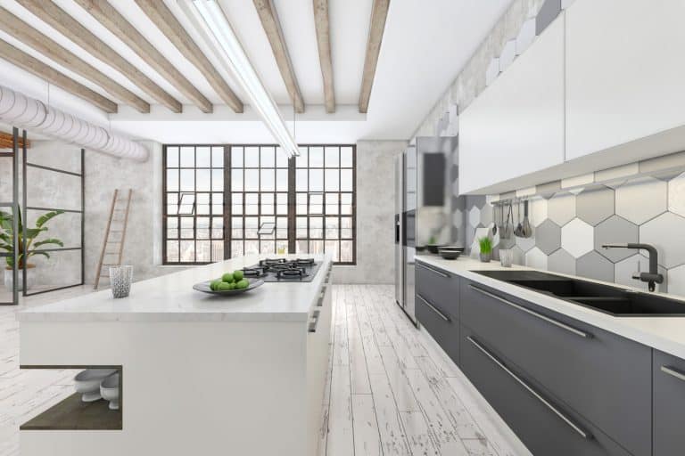 Large modern kitchen interior with white kitchen counter. Grey tiled wall, parquet, sink, window and concrete wall in the background