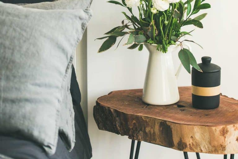 Trendy Scandinavian style bedroom interior with washed linen gray pillows and wooden nightstand with bucket of flowers and candle, 11 Unusual Bedside Tables