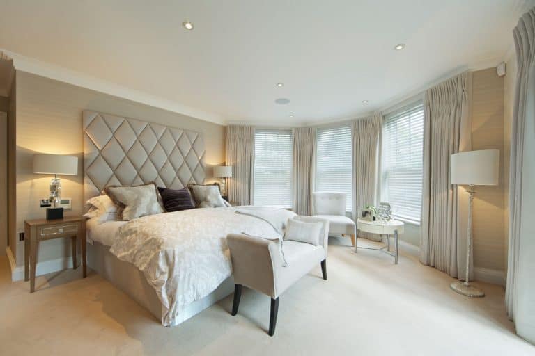 Spacious contemporary bedroom with cream carpeted flooring, white curtains on the bay window section, and floor lamps on each corner, 11 Awesome Bedroom Floor Lamps Ideas