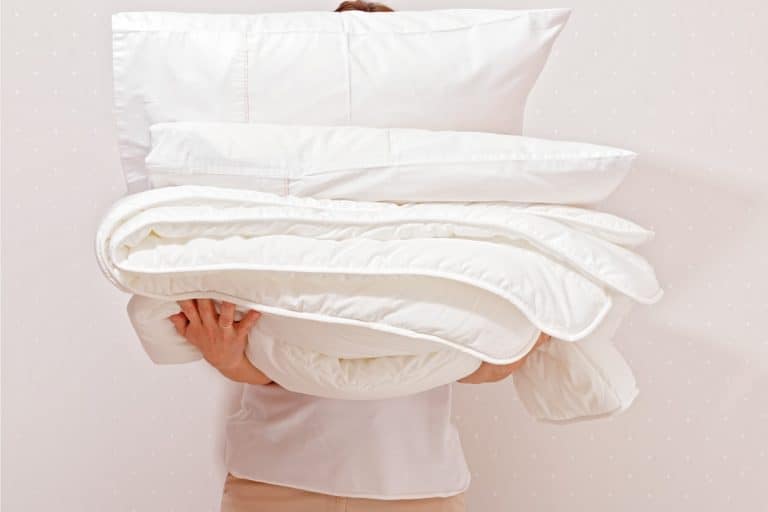 Lady holding a pile of pillows and bedsheets, Can You Wash Pillows In A Washing Machine?