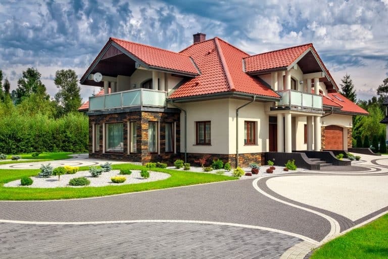 一个luxurious huge mansion with red asphalt roofing, gorgeous lawn with small plants, and a patterned driveway, 21 Paver Driveway Ideas To Consider