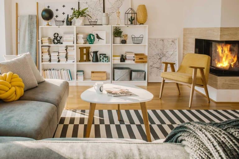 Wooden rack with books and decorations in Scandinavian living room interior with fireplace, coffee table and corner sofa, 11 Living Room Layouts With A Corner Fireplace To Inspire You