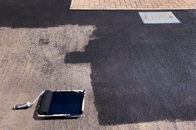 一个roller being used to apply asphalt sealant on the driveway, Should A Driveway Be Dry Before Sealing It? [And How Long To Wait!]