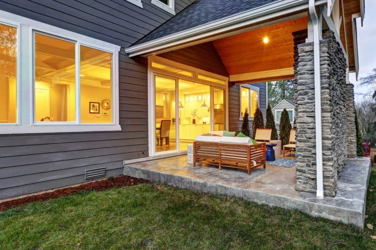 Back porch of a huge mansion with gray wooden sidings and a nicely lit interior with a back porch with stone decorative cladding, 15 Back Porch Ideas You Should See!
