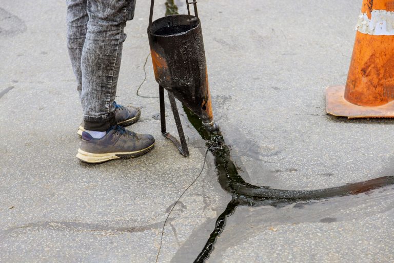 Man sealing asphalt driveway with filled cracks sealcoating selective focus,How Much Driveway Sealer Do I Need?