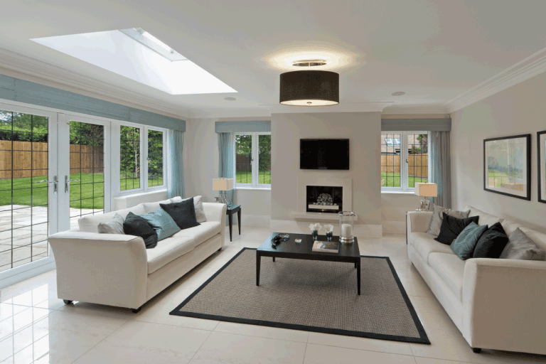 A slightly angled view of a bright and spacious lounge in an expensive new home with large leaded glass windows, How Much Space Between Furniture For Walking?