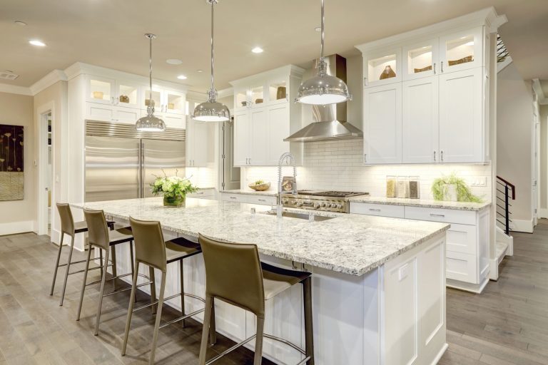 White kitchen design features large bar style kitchen island with granite countertop illuminated by modern pendant lights, 12 Great White Granite Countertop Ideas