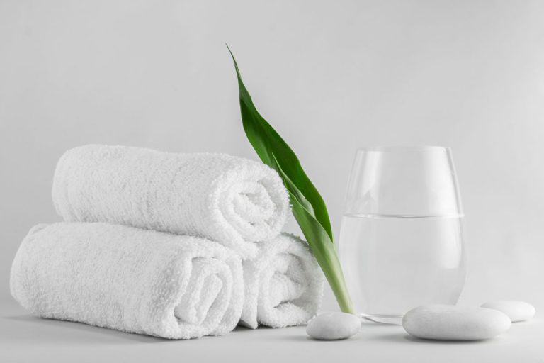 Spa setting decorated with green leave towel and white stone, What Color Towels For A Beige Bathroom? [6 Great Ideas!]
