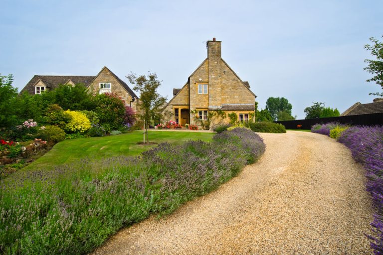 English village with a house nearby and a set of mixed flowers near the gravel driveway, How Wide Should A Gravel Driveway Be?