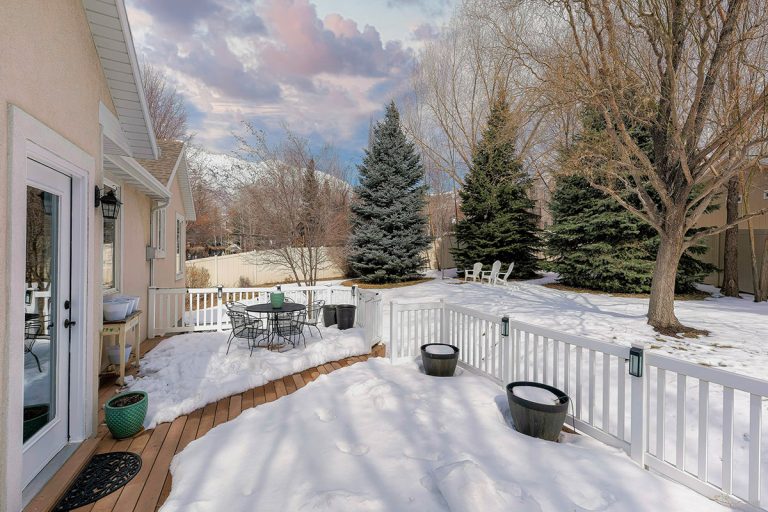 Snow covered deck of a house with white railing and wood planks, Should You Shovel Your Deck? [And How To]
