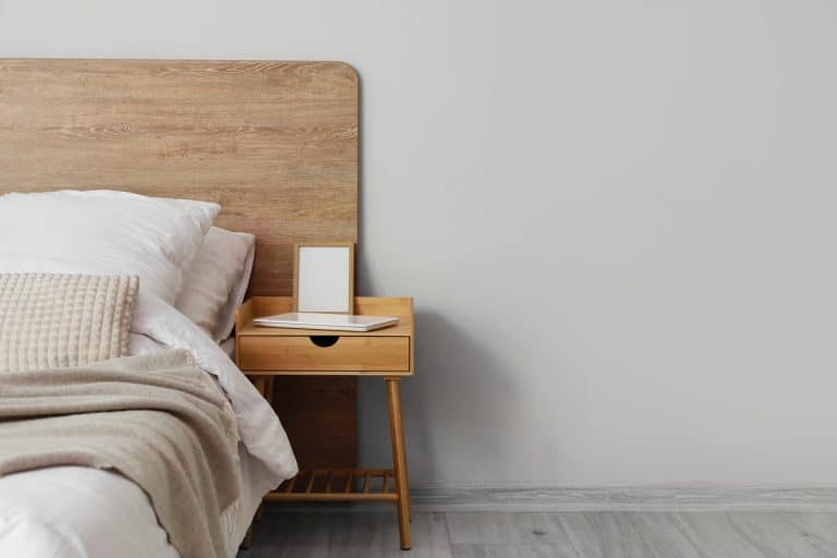 A wooden bedside table with a laptop on top and an empty picture frame, Can Nightstands Be Used As End Tables? [& How To]