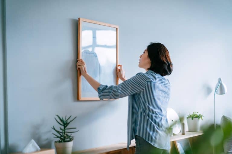 Decorator hanging picture on white brick wall in room. Interior design - How Much Weight Can Drywall Hold [Is It Enough For Your Home Project]
