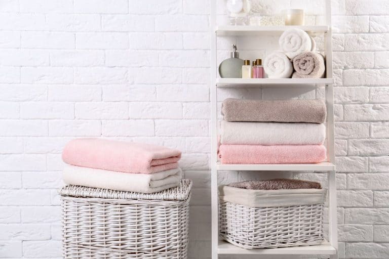 Shelving unit and baskets with clean towels and toiletries near brick wall. - How To Decorate A Bathroom With Towels In A Basket